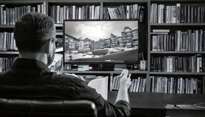 person watching a streaming service with an encyclopedia in one hand and a remote in other