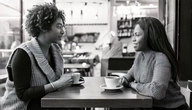 two people in a coffee shop having a discussion about their different viewpoints amicably