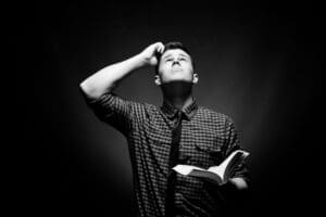 Well dressed man holding a Bible and looking up at God in confusion in grayscale