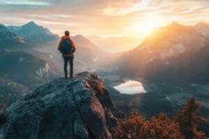 hiker standing on mountain peak overlooking valley at sunrise. breathtaking landscape with serene lake and rugged mountains. adventure, exploration, travel, nature poster.