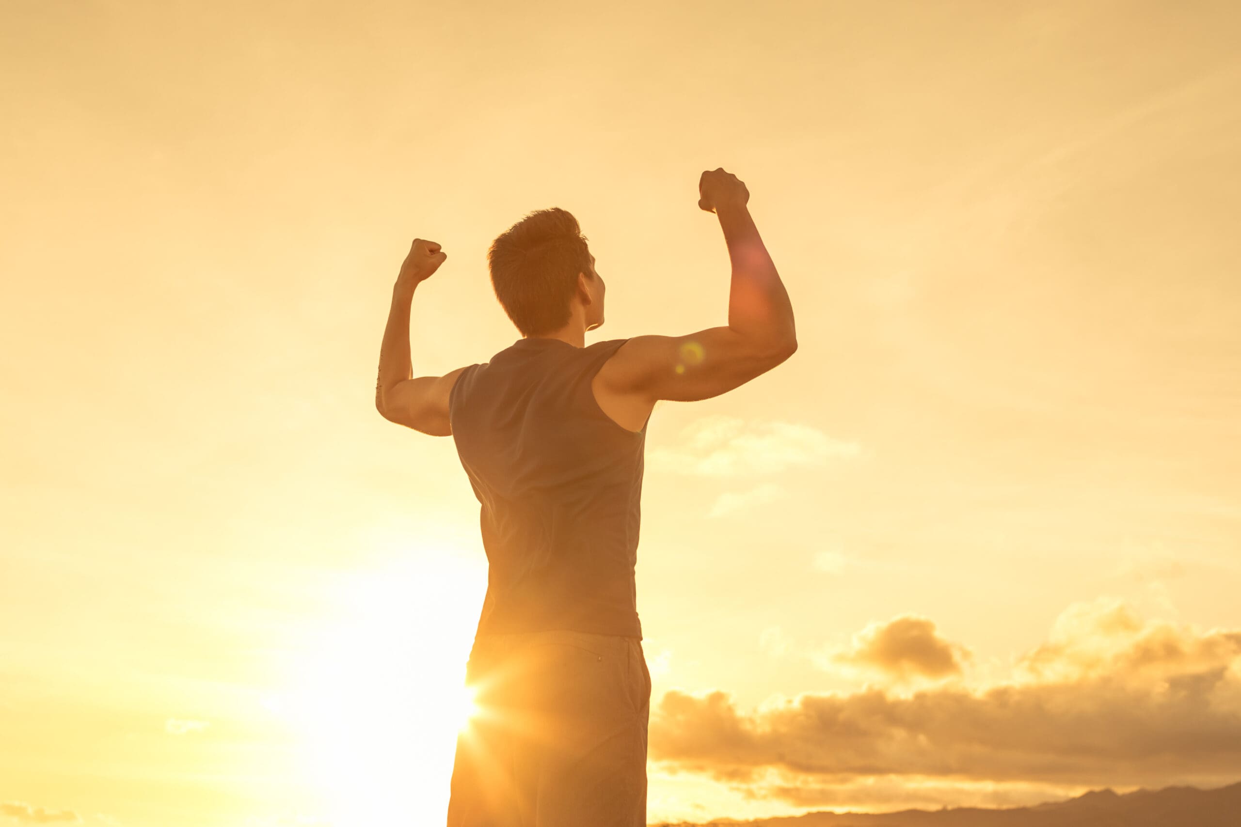 Strong confident man flexing his arms facing the sunset.